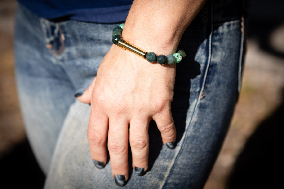 Hand wearing a cremation bracelet  with moss agate and flower beads, resting on a blurred background